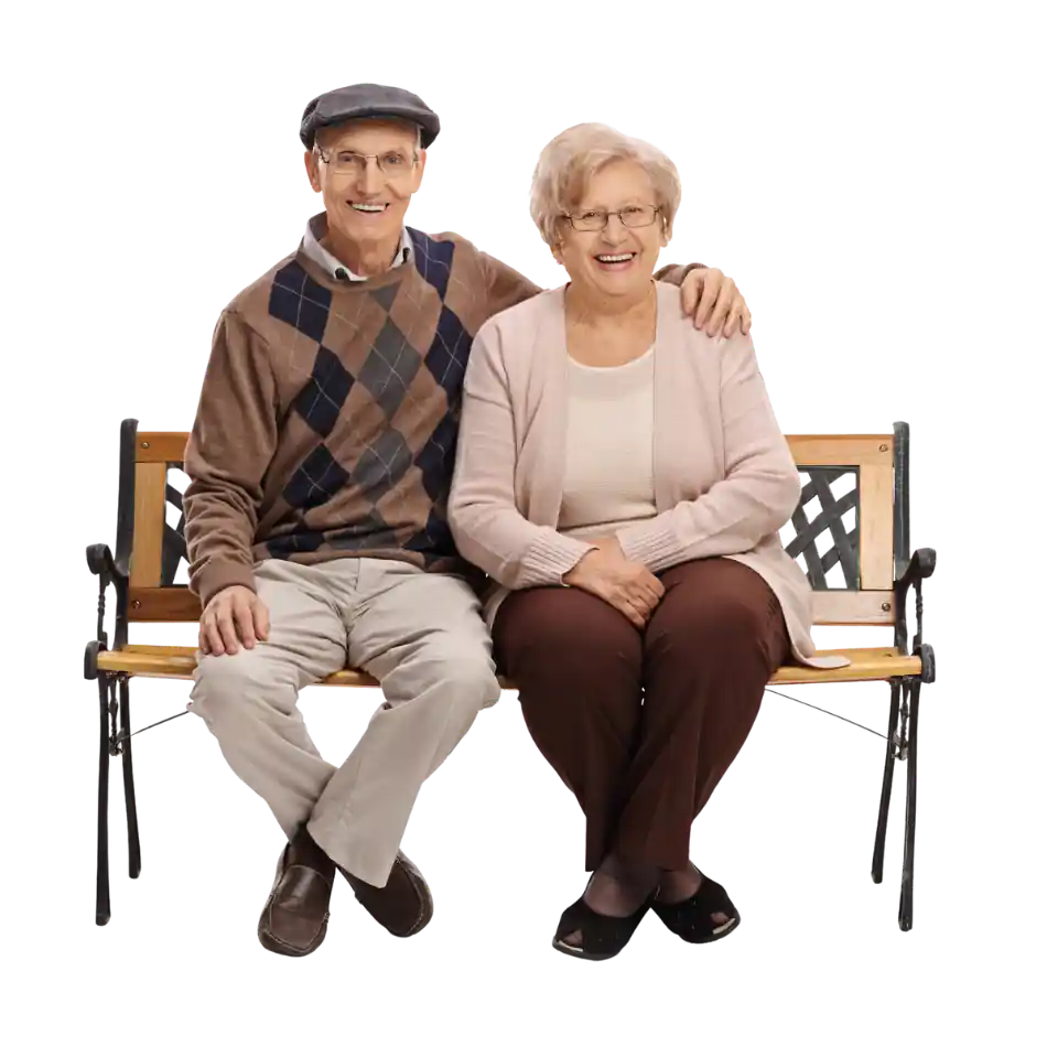 An elderly couple is sitting on a bench smiling.